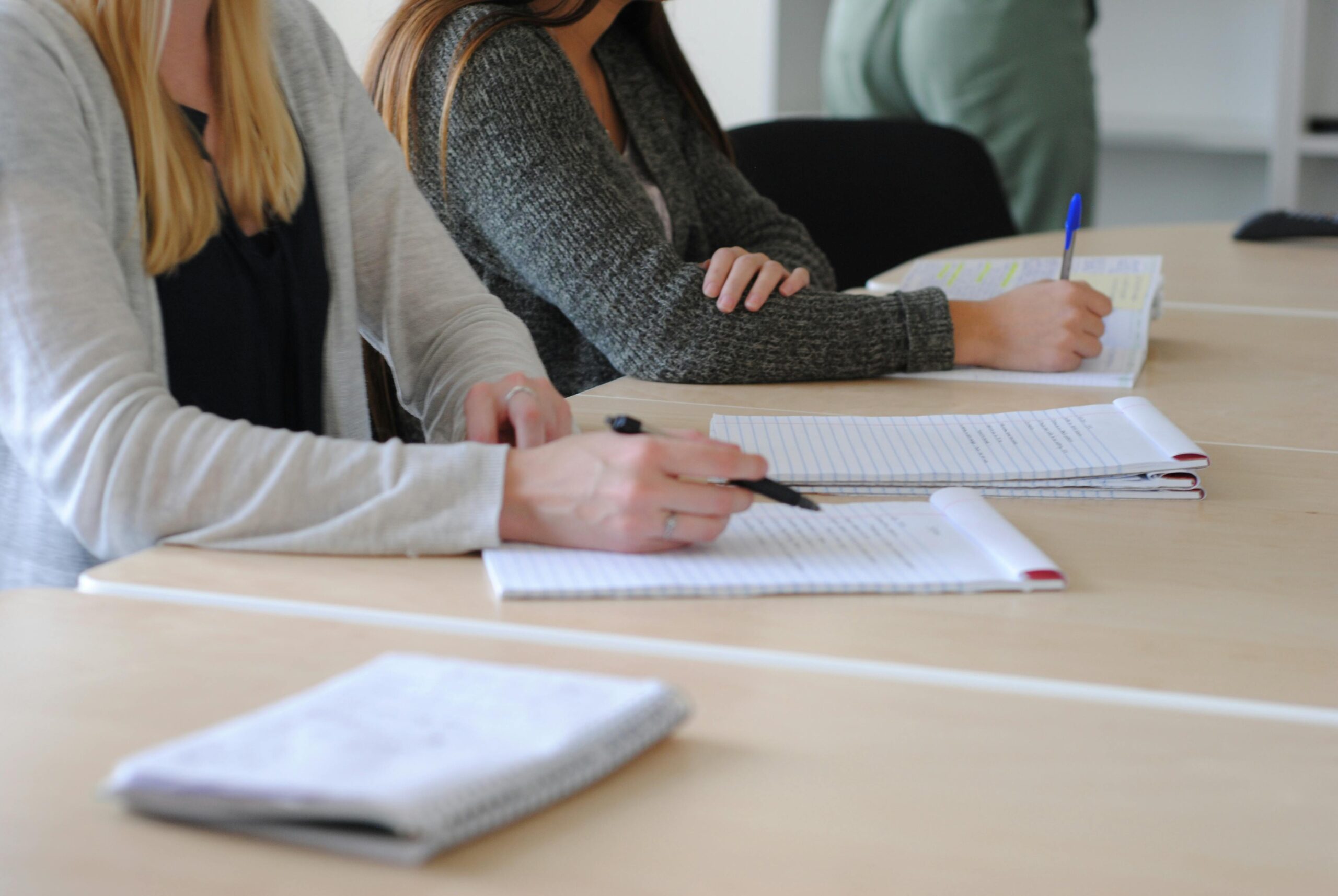 Group of students writing notes at a meeting in a well-lit classroom.